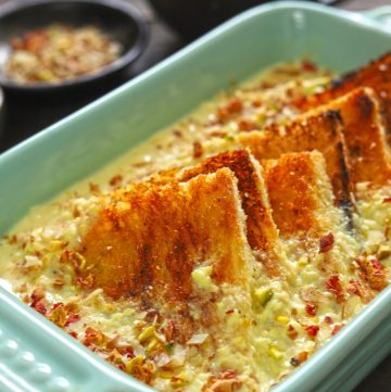 Side shot of baked shahi tukra in a green ceramic baking dish.