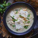 aerial shot of paneer in white gravy on a black serving bowl