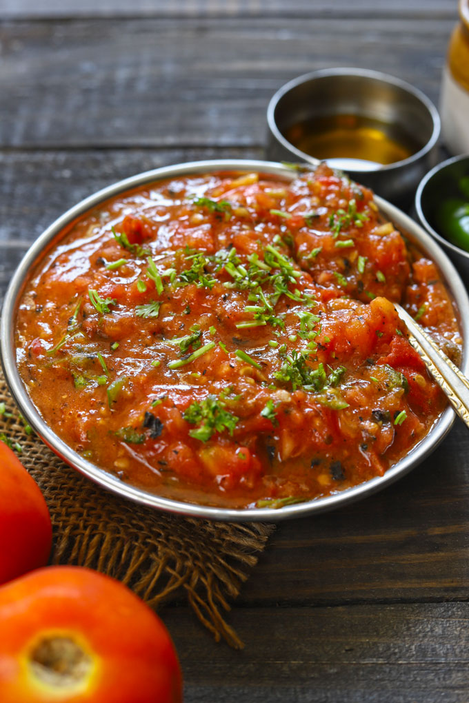 side shot of roasted tomato chutney in a steel bowl with a spoon