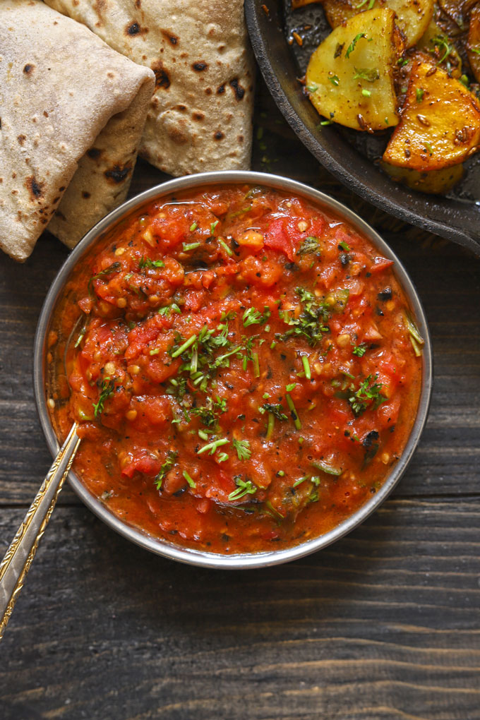 aerial shot of roasted tomato chutney in a steel bowl with a spoon