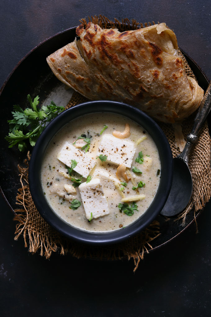 aerial shot of paneer in white gravy on a black serving bowl