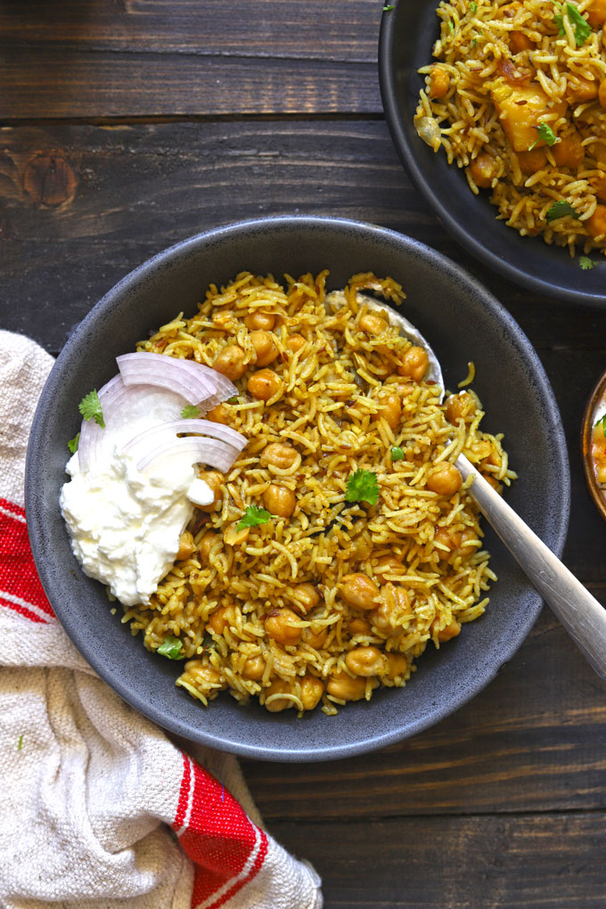 aerial shot of chana pulao in a black ceramic bowl with curd and onion