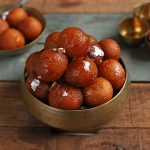 side shot of gulab jamuns stacked on a brass serving bowl