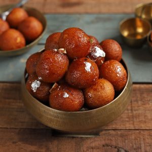 side shot of gulab jamuns stacked on a brass serving bowl