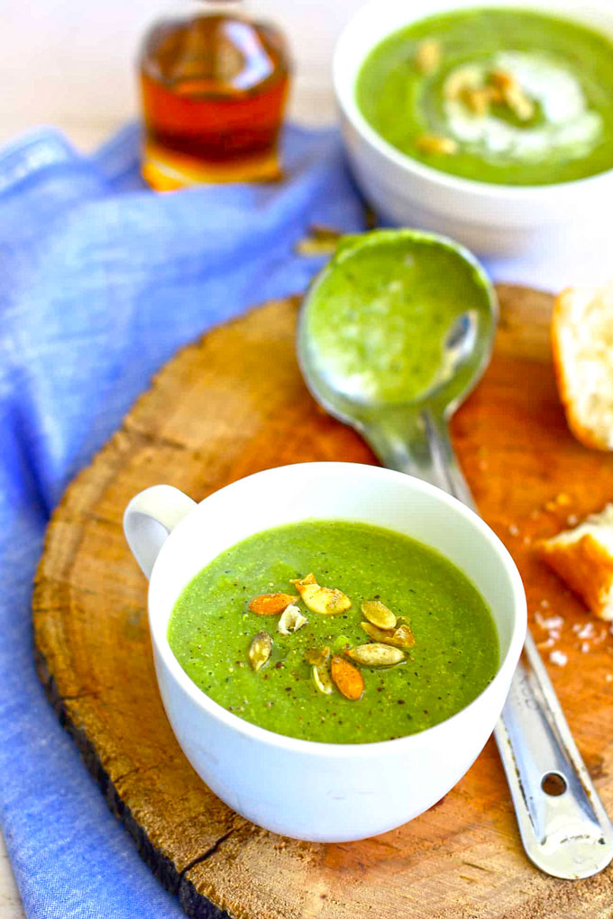 side shot of broccoli soup in a white mug with blurred soup ladle in the background