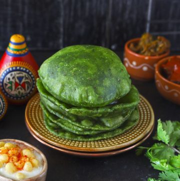 side shot of palak poori stacked on a brown serving plate