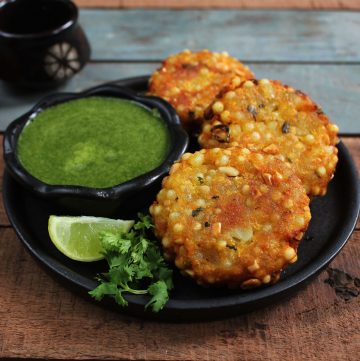 side shot of sabudana vada arranged on a black serving plate with green chutney in a bowl