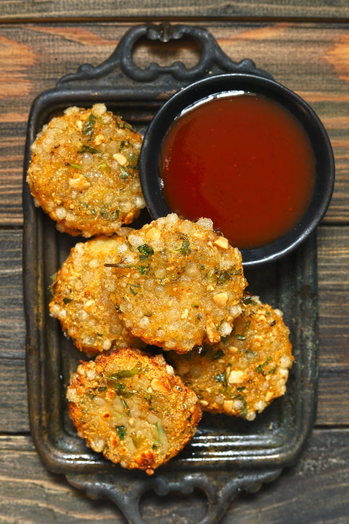 aerial shot of sabudana vada in a black tray with tomato ketchup in a black bowl