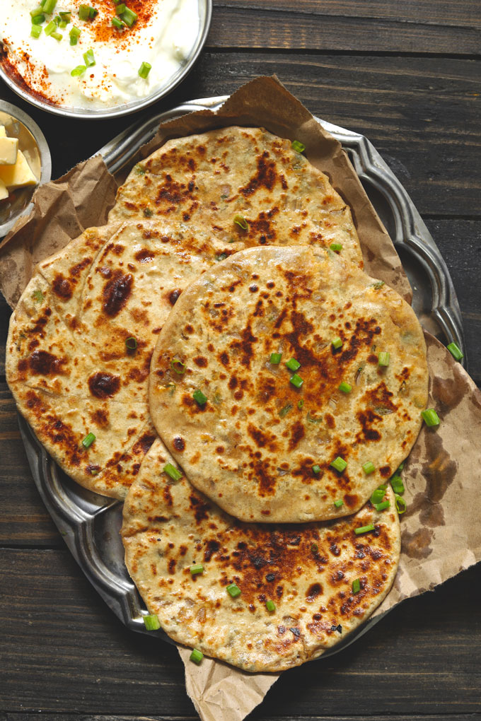 aerial shot of spring onion and paneer paratha stacked on a steel platter