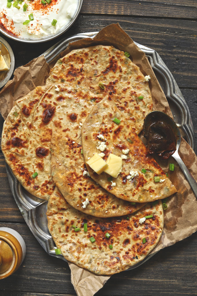 aerial shot of paneer paratha with a dollop of butter stacked on a steel platter