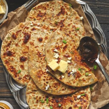 aerial shot of paneer paratha with a dollop of butter stacked on a steel platter