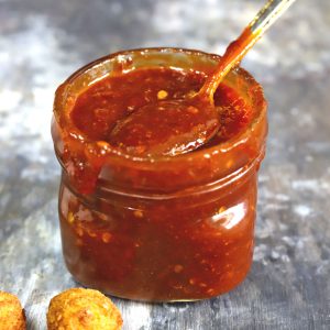 side shot of sweet chilli sauce in a glass bottle with a spoon