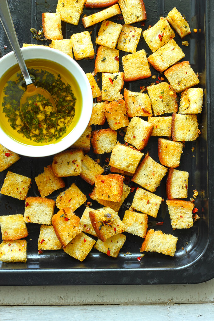 aerial shot of bread croutons on a black baking tray with a bowl of olive oil