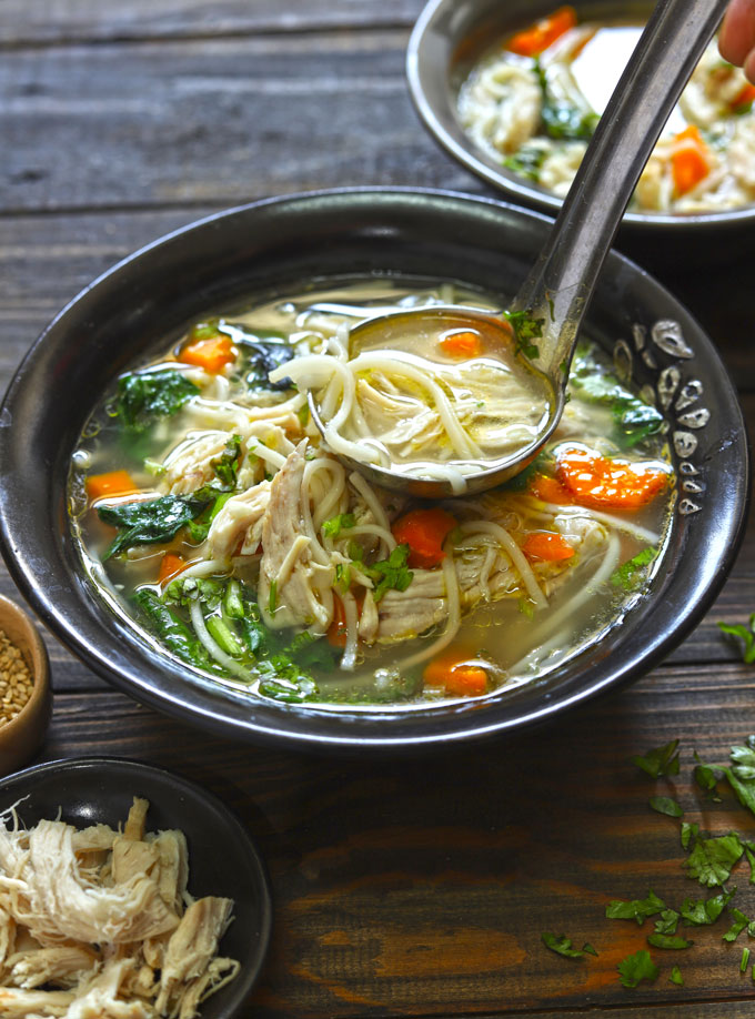 side close up shot of chicken soup in a black ceramic bowl with a ladle