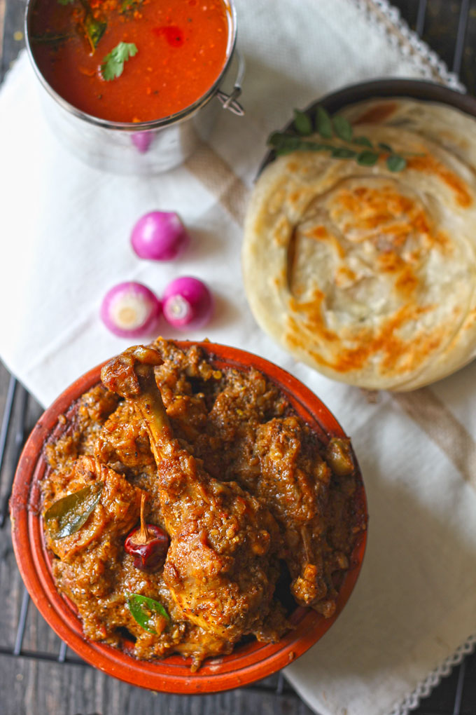 aerial shot of Chettinad chicken in an earthen serving bowl with parotta and tomato rasamv