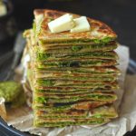 side close up shot of matar paratha stacked on a black plate topped with butter