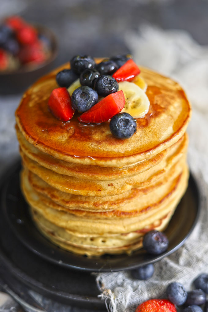 side shot of healthy pancakes stacked on a plate topped with fresh berries