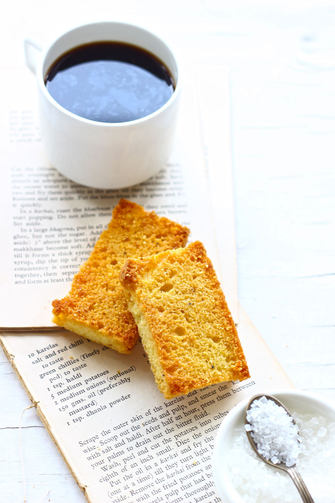 side shot of two pieces of cake rusk stacked on a white surface with a cup of coffee