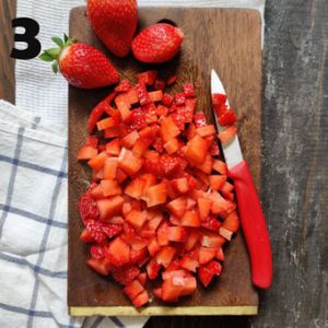 aerial shot of chopped strawberries on a wooden board with a red knife on the side