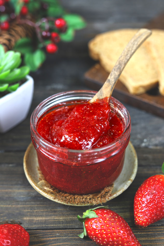 side shot of strawberry jam in a glass jar with a wooden spoon