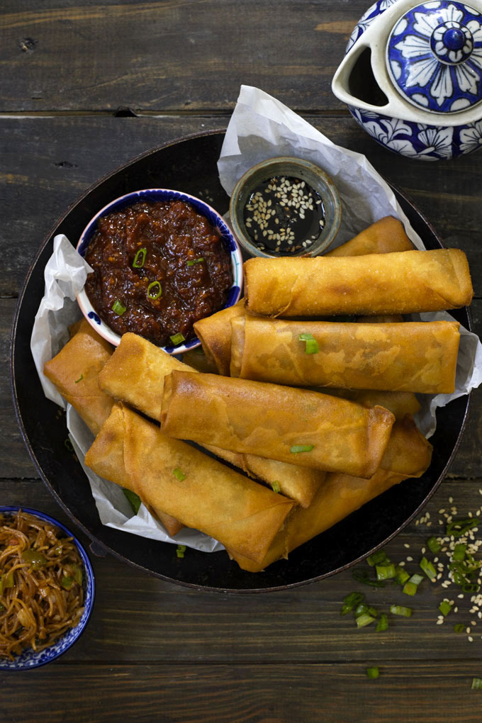 aerial shot of spring roll stacked in a black platter with red chili sauce