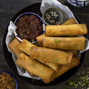 aerial shot of veg spring roll stacked in a black platter with red chili sauce