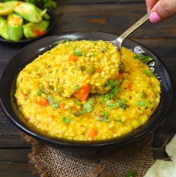 side close up shot of dalia khichdi in a black bowl with serving spoon