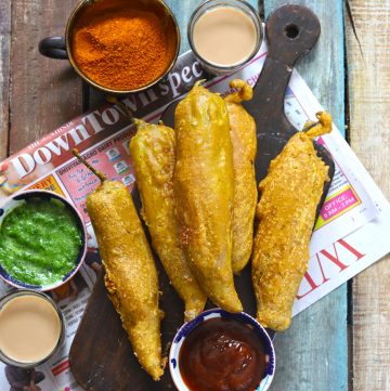 aerial shot of chilli bajji stacked on a brown wooden platter with tea, and chutney