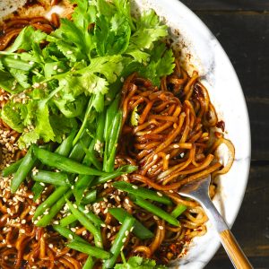 aerial close up shot of chili oil noodles in a bowl with fork and lot of fresh greens