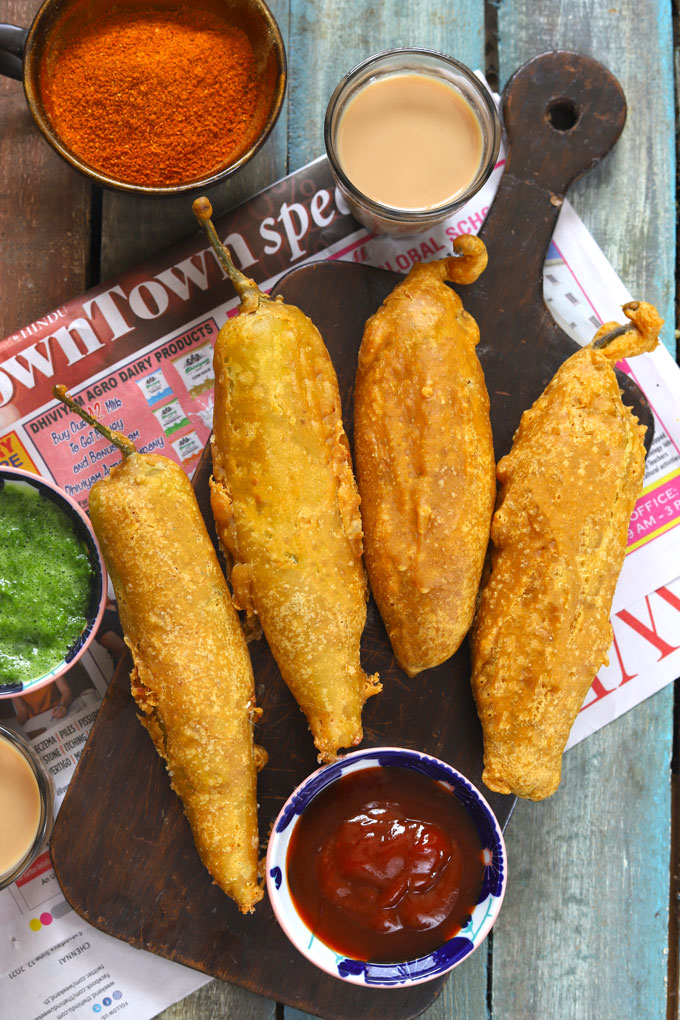 aerial shot of chilli bajji stacked on a brown wooden platter with tea, and chutney