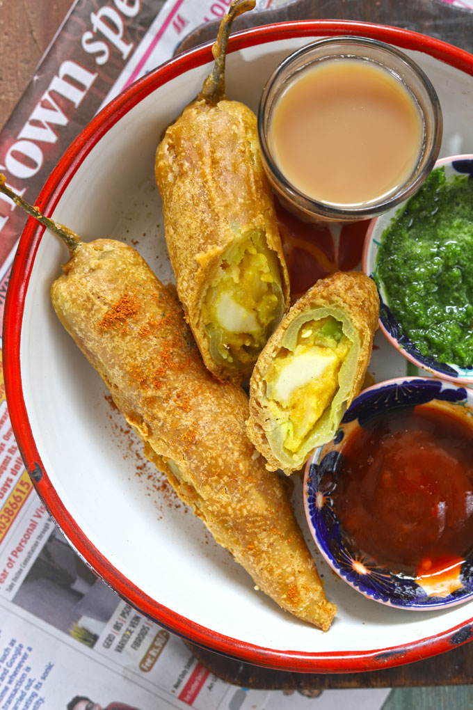 aerial shot of stuffed chilli bajji on a white plate with tea and chutney