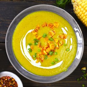 aerial shot of creamy corn soup in a grey ceramic bowl with garnish of cream, green onion, and roasted corn
