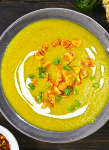 aerial shot of creamy corn soup in a grey ceramic bowl with garnish of cream, green onion, and roasted corn