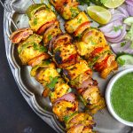 aerial shot paneer tikka skewers stacked on a vintage platter with green chutney and salad