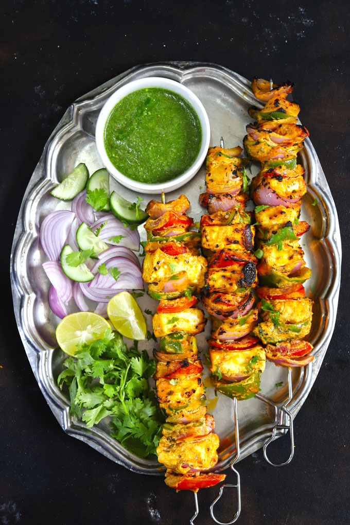 aerial shot paneer tikka skewers stacked on a vintage platter with green chutney and salad