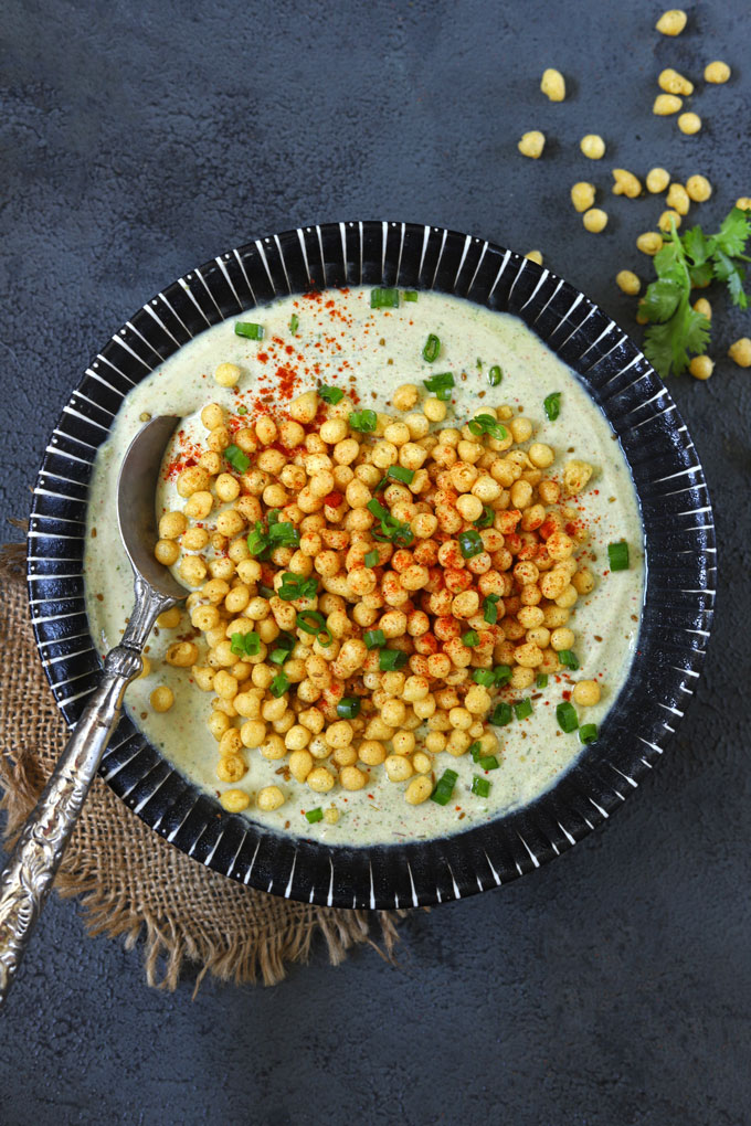 aerial shot of spring onion boondi raita in a black ceramic bowl