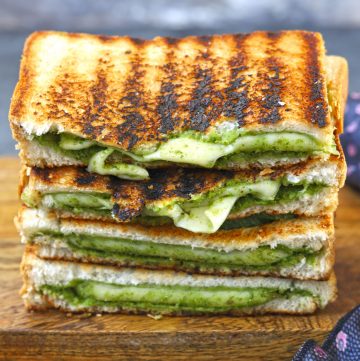 side shot of sliced cheese chutney sandwich stacked on a wooden platter