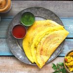 aerial shot of moong dal cheela arranged on a metal platter with ketchup and green chutney