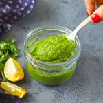 side close up shot of mint chutney in a glass jar with spoon scooping out the chutney