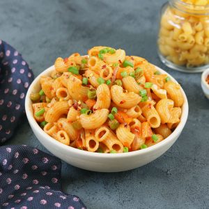 side shot of masala macaroni in a white bowl on a grey surface