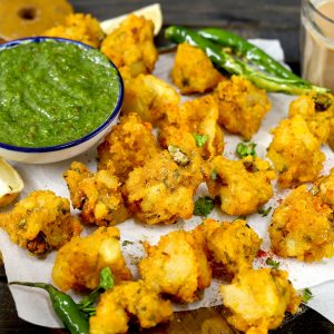 side shot of aloo pakora stacked on a platter with chutney