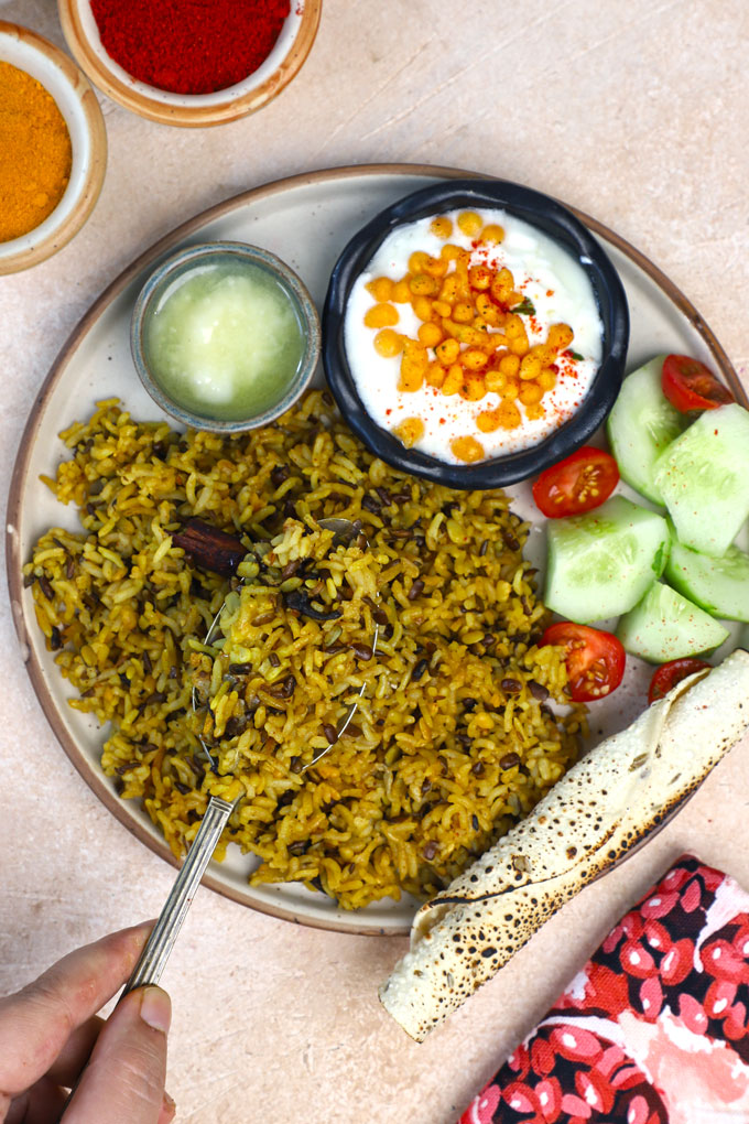 aerial shot of urad dal khichdi on a ceramic platter with curd, salad, and ghee