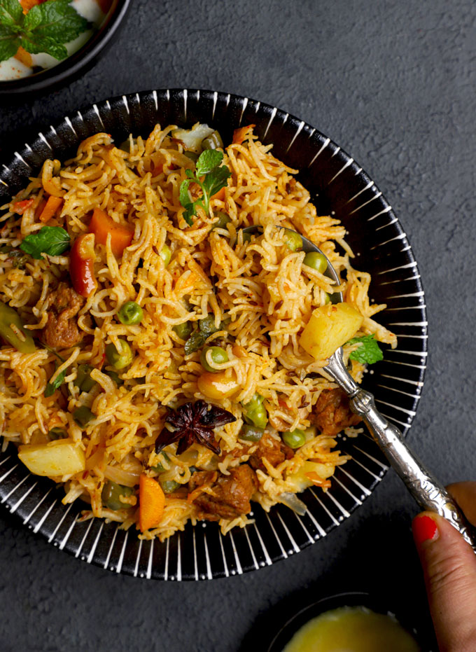 aerial shot of vegetable pulao in a black ceramic bowl with spoon