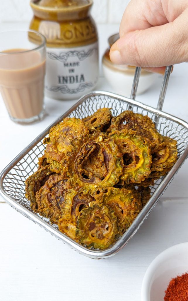 side shot of air fryer karela chips stacked on a wire basket