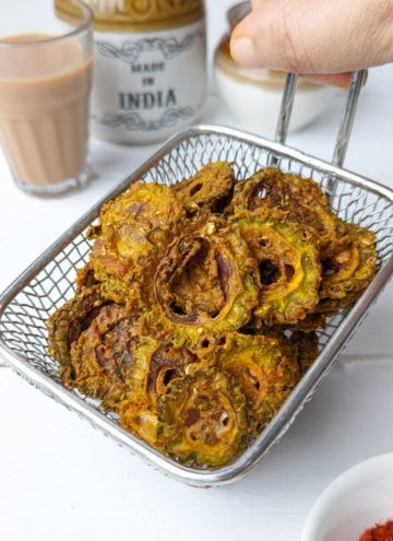 side shot of air fryer karela chips stacked on a wire basket