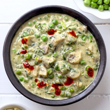 aerial shot of mushroom methi matar malai in a black ceramic bowl.