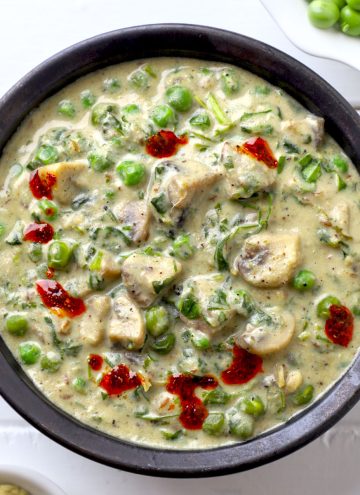 aerial shot of mushroom methi matar malai in a black ceramic bowl.
