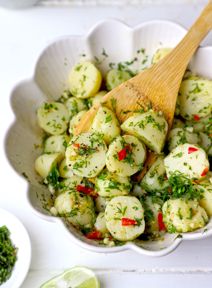 side angle shot of potato salad in a white ceramic bowl with the wooden spoon