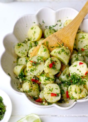 side angle shot of potato salad in a white ceramic bowl with the wooden spoon