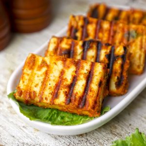 side shot of grilled paneer served on a white platter